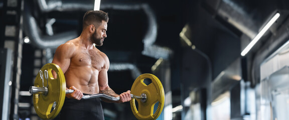 Handsome naked weightlifter lifting heavy barbell in gym, free space, panorama