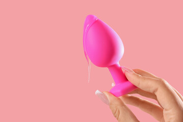 Woman holding anal plug with lubricant on pink background, closeup