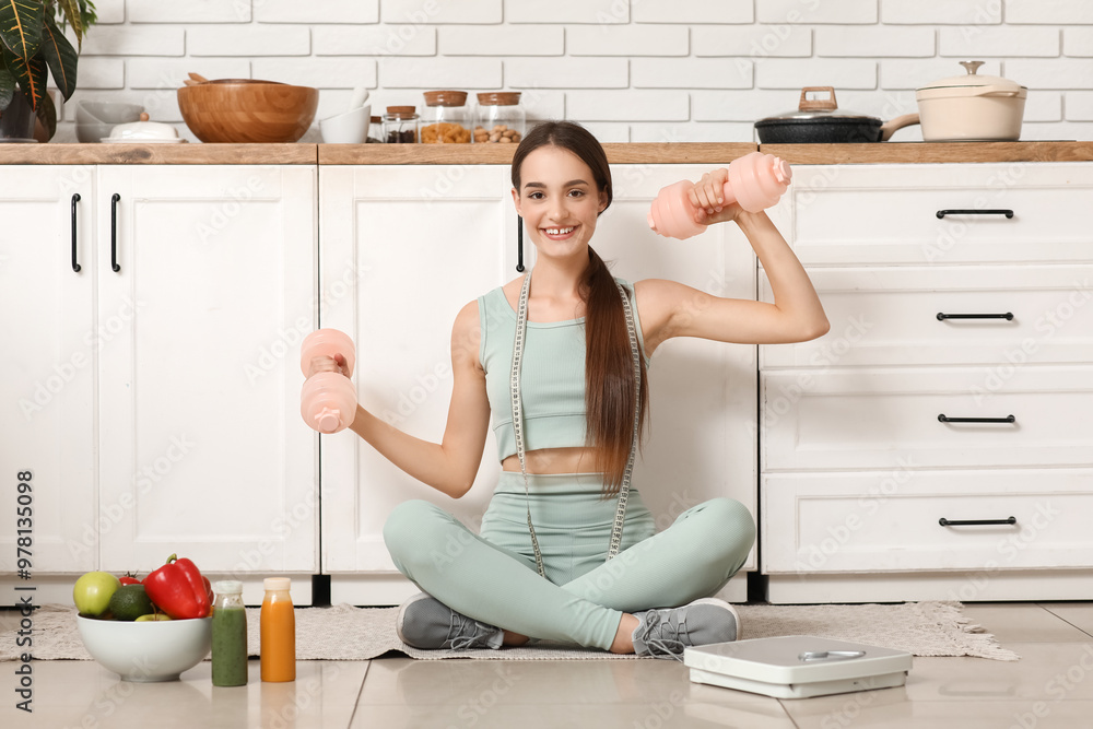 Poster Sporty young woman with dumbbells sitting on floor in kitchen. Diet concept