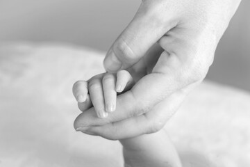 Black and white image of a close up of an infant's hand held by a mother's hand wearing a wedding ring.