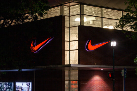 Portland, Oregon, USA-May 15, 2019: Nike retail shop store with its big illuminated logo signage banner at the facade of the shop. Captured at night. High quality picture for download.