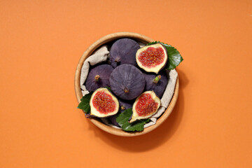 Fresh ripe figs in a wooden bowl on an orange background