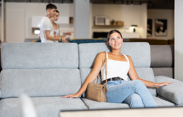 Obraz premium Young woman chooses comfortable sofa in department of furniture store