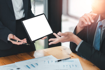 Professionals discussing financial data with a digital tablet and documents in a modern office setting.
