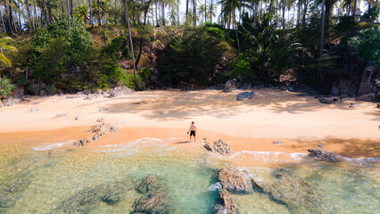 Man relex,aerial view of the tropical island Thailand with a white sandy beach with palm trees and big black boulder stones in the ocean.j