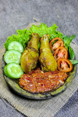 Ayam penyet (smashed fried chicken) is Indonesian East Javanese cuisine, served with sambal chili, lettuce and cucumber slice. Indonesian Spicy Chicken with Various Vegetable