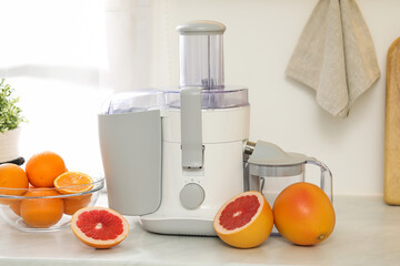Modern juicer and grapefruits on white counter in kitchen