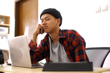 Overworked Asian man sitting at workplace placing head on hand feeling tired