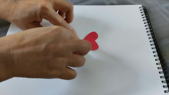 Una toma de cerca de una persona pegando con las manos una nota con el texto lo siento cerca de un coraz&oacute;n de papel rojo  en una hoja de color blanco