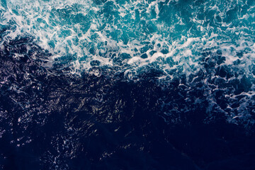 Aerial shot capturing the contrast between dark ocean waves and bright white seafoam, creating...