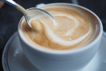 A closeup view showcasing a creamy coffee with beautiful swirls and a spoon resting in a white cup