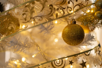 una esfera dorada enmarcada por cinta decorativa en árbol de navidad blanco 