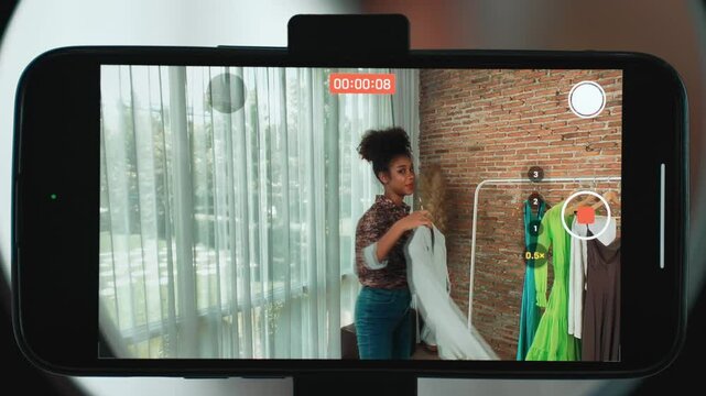 Rear view behide smartphone screen recording woman influencer shoot live stream vlog video review clothe crucial social media or blog. Girl with apparel studio lighting for marketing broadcast online