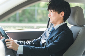 車を運転するスーツ姿の若い男性ビジネスマン

