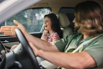 Couple arguing inside a car with visible frustration and tension, passenger showing distress and...