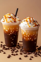 Two iced coffees in plastic cups with cream and caramel on top, on a beige background