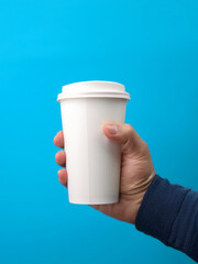 A product mockup in a hand holding a cup, with a white space in it for branding or logo placement, simple blue color background, no text, high quality