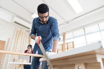 Asian male carpenter working and cutting piece of wood at wood workshop