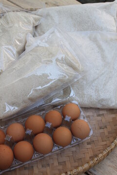 Rice, sugar and eggs in woven bamboo called tampah on a wooden table

