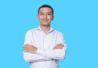 Portrait of confident smiling Asian young man wearing shirt standing with arms folded isolated on blue background.