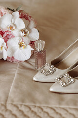 A bouquet of white flowers sits on a bed next to a purse and a bottle of perfume