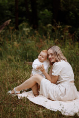 Fototapeta premium Woman sitting on the grass with a child in her arms. Relaxation or picnic in a summer park. Mother and child concept.