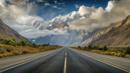Naklejka premium Cloud-covered Passu Cones stand tall as the Karakoram Highway winds through the peaceful Hunza Valley, with the road stretching into the distance.