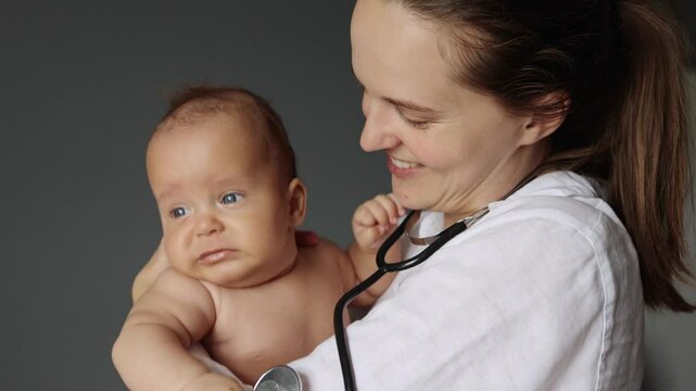 Newborn physical exam. First moments of bonding. Professional doctor pediatrician caressing and calming down crying infant baby boy or girl in hospital