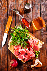 Raw beef meat chopped in cubes with bunch of fresh parsley on wooden cutting board for cooking