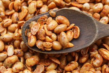 close up of peanuts with spicy seasoning on wooden spoon. background on pile of peanuts. peanut snack