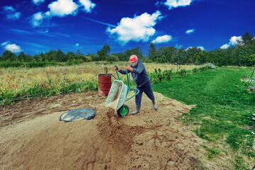 Worker pours sand from wheelbarrow onto concrete ring of septic tank.