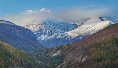 Fototapeta premium Autumn landscape, mountain valley, snow-capped peaks in the clouds