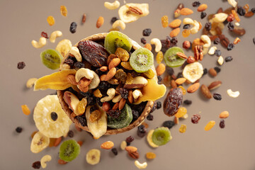 Dried tropical fruits with various nuts and raisins on a beige background.