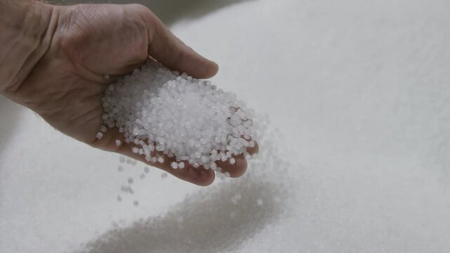 Slow motion footage of a hand picking up and holding then dropping white plastic pellets in a factory.