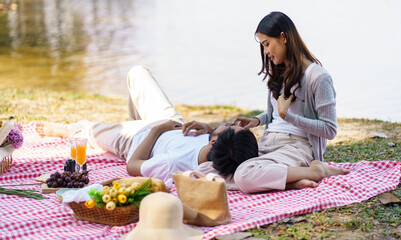 Happy romantic asian couple lying down at the park picnic time in summer holidays vacation.