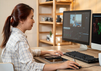 Female asian freelancer editing video for customer or travel blogger in program on computer while sitting at the table and working at home