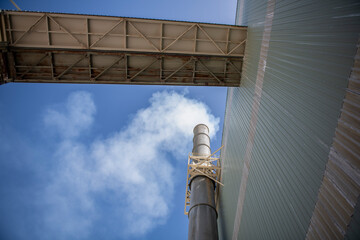 Steam smoke rising from smokestack next to enclosed conveyor belt