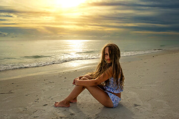 Beautiful young girl sitting in sand at sunset Anna Maria Island