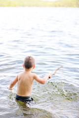 Fototapeta premium Young boy splashing in lake water while holding a large stick.