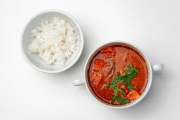 Bowl of curry with pieces of meat and a side of steamed rice arranged neatly for a meal