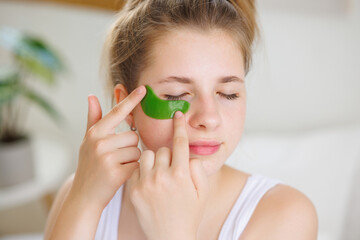 Woman applying green under-eye patch for skincare