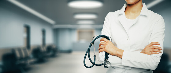 Close up of folded doctor hands with stethoscope on blurry wide corridor interior background with...