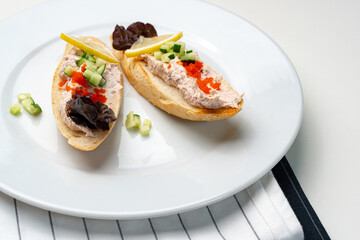 Tasty open-faced sandwiches with tuna spread, topped with fresh vegetables and lemon slices on a white plate