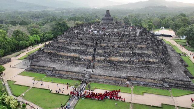 A serene aerial view captures monks peacefully praying at Borobudur Temple, the largest Buddhist monument. The footage highlights their ritual practices in front of the ancient stone architecture.