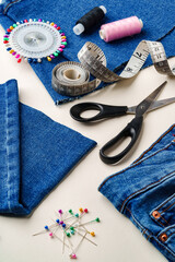 Sewing supplies and denim fabric arranged on a workspace for clothing alterations in a bright...