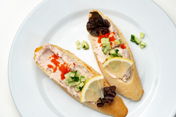 Tasty open-faced sandwiches with tuna spread, topped with fresh vegetables and lemon slices on a white plate