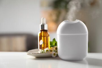 Essential oil diffuser, cosmetic product and chamomile flowers on white table at home