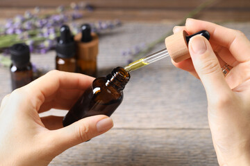Woman using essential oil at wooden table, closeup