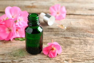 Geranium essential oil in bottle, pipette and beautiful flowers on wooden table, closeup. Space for text