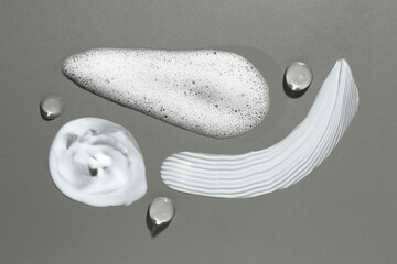 Smears of different cosmetic products on grey background, top view